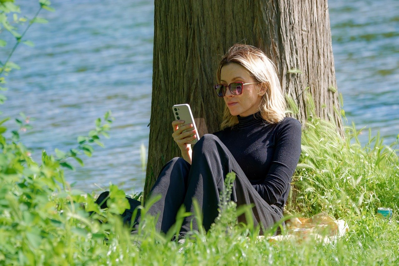 女子坐在樹下滑手機